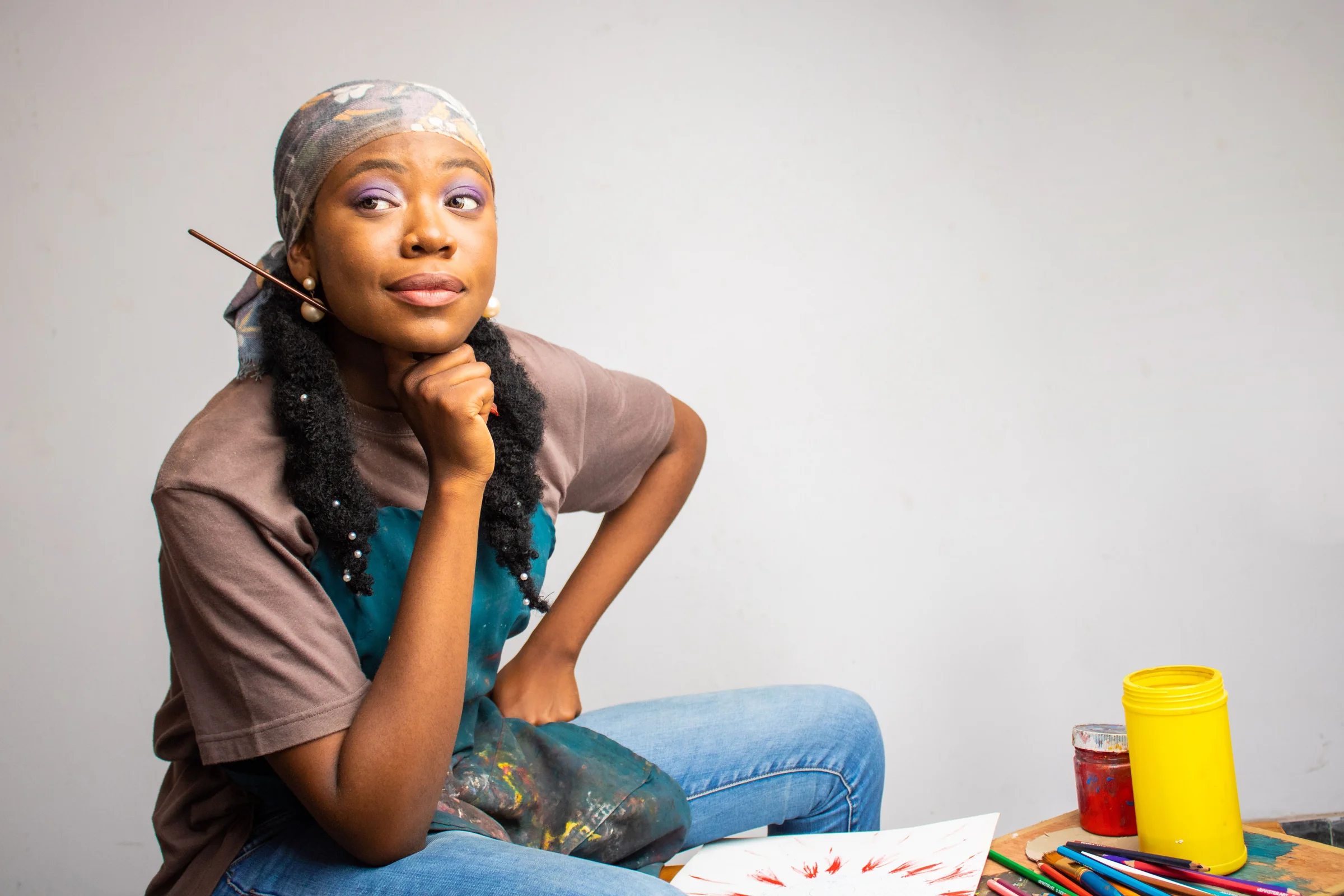 An artist holding a paintbrush beside her paints and work